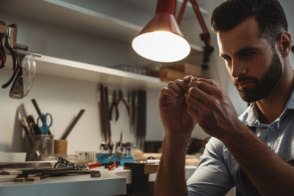 Perfection. Close up of young male jeweler looking and inspecting a ring at his jewelry workshop