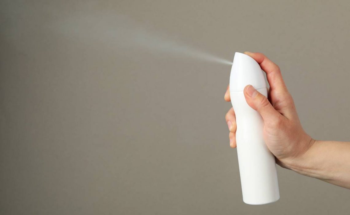 Woman spraying deodorant on gray background, space for text