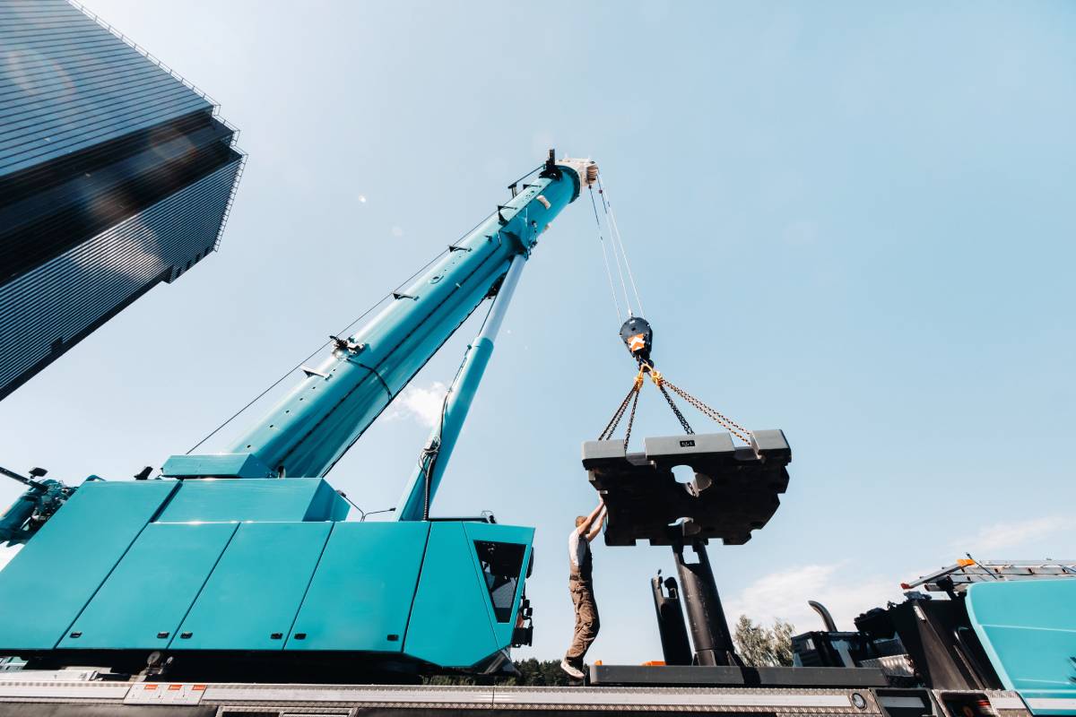 the counterweight is installed by an unrecognizable worker on a large blue car crane and is prepared to work on a site next to a large modern building. The largest truck crane for solving complex tasks.