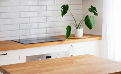Wooden tabletop with free space for product montage or mockup against blurred white kitchen with cutting board and plant in scandinavian style in morning light