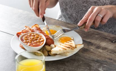 Woman having english breakfast with fried eggs, sausages, and baked beans