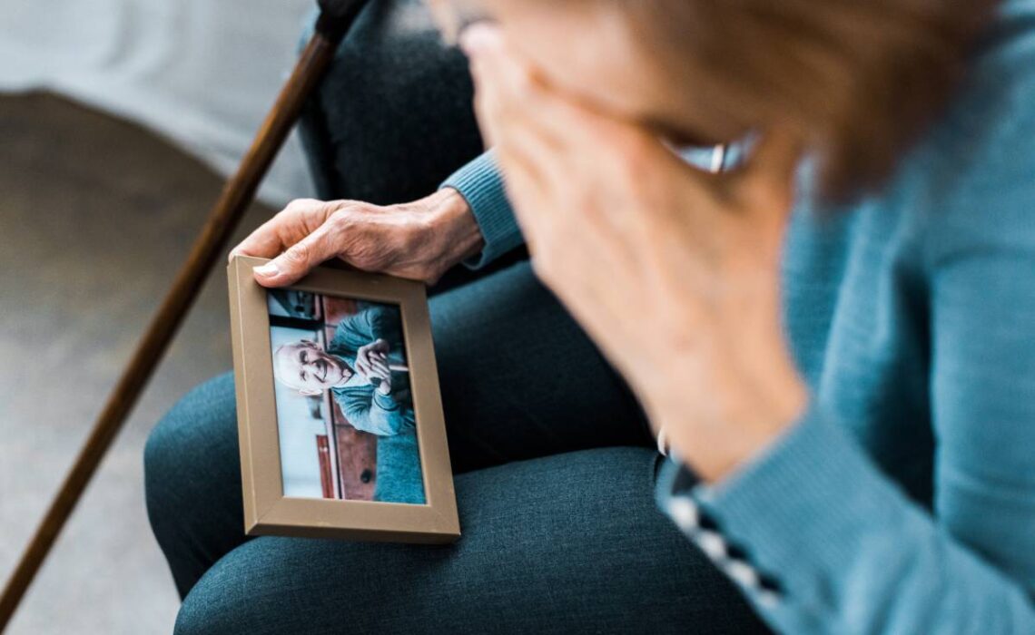 senior woman covering face with hand and crying while looking at frame with man on photograph