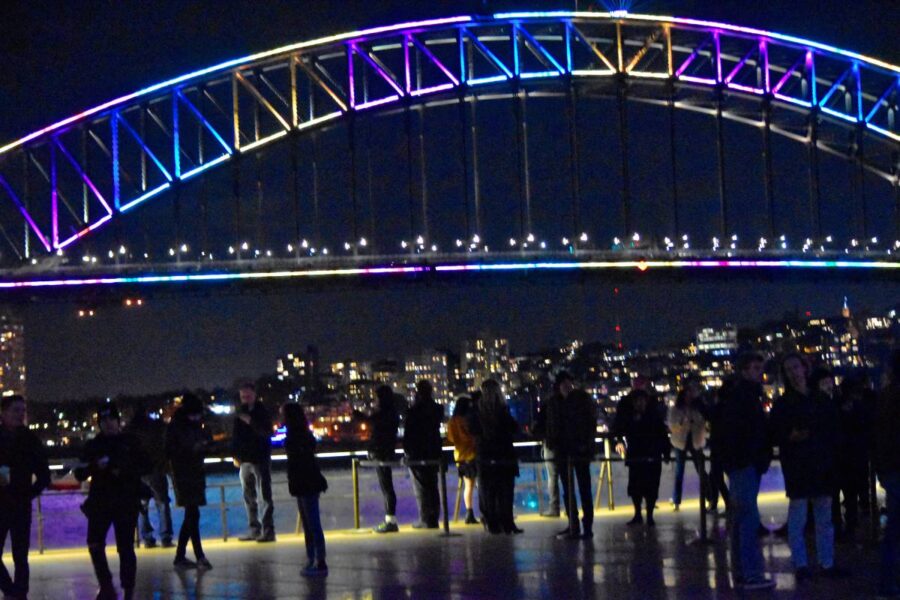 Colorful Silhouettes of people watching the neon lights of Vivid across from the Harbor bridge in front of the Sydney Opera House night life. Nightlife. People at night. Life at night.